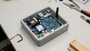 Centrale d’alarme domestique ouverte montrant un module de communication cellulaire, un emplacement pour carte SIM M2M, une carte électronique, des câbles et une antenne.
